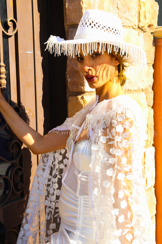 Woman wearing a white lace dress and hat against a stone wall.